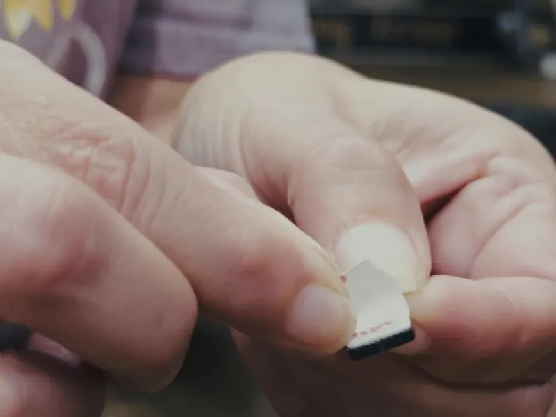 Fingers holding a peel-and-stick Popper Top tab